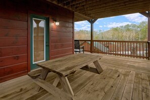 A wooden deck with a picnic table, a door with a green frame, and a chair. - Bear Cove Lodge Cabin Rental (Pigeon Forge)