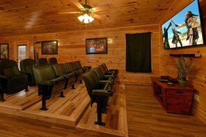 A wooden interior with a ceiling fan, framed pictures, a television, and a row of chairs. - Bear Cove Lodge Cabin Rental (Pigeon Forge)