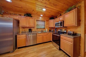 A kitchen with wooden cabinets, a stainless steel refrigerator, a microwave, and a stove. - Bear Cove Lodge Cabin Rental (Pigeon Forge)