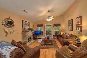 A cozy living room with a fireplace, leather sofas, a television, and a ceiling fan. - Bear Paw Chalet Cabin Rental (Pigeon Forge)