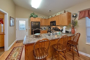 A kitchen with wooden cabinets, a refrigerator, a microwave, a sink, and a bar area with chairs. - Bear Paw Chalet Cabin Rental (Pigeon Forge)
