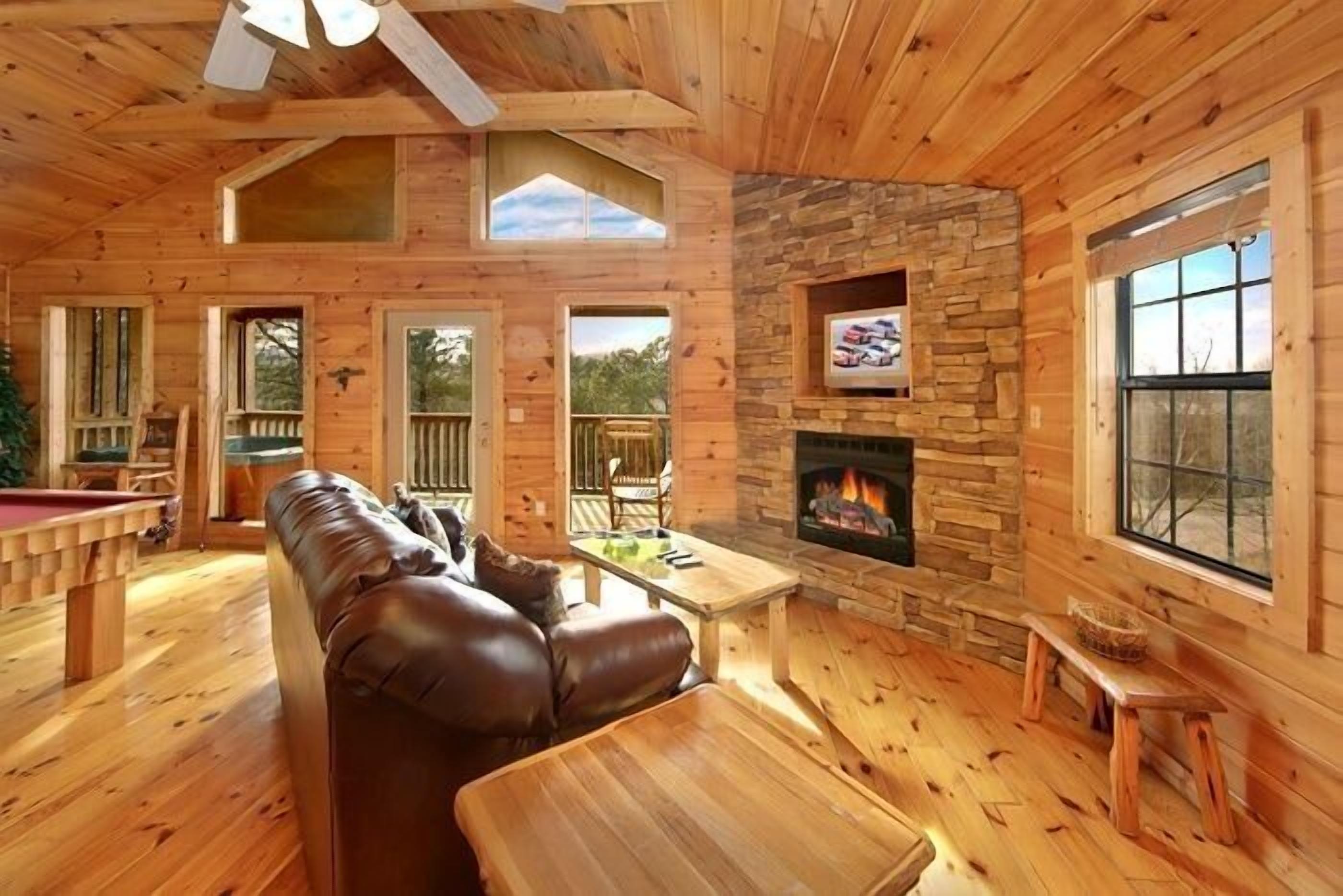A wooden cabin interior with a stone fireplace, leather sofa, and a pool table.