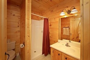 A wooden cabin bathroom with a toilet, shower, sink, and mirror. - Bear Tracks Cabin Rental (Pigeon Forge)