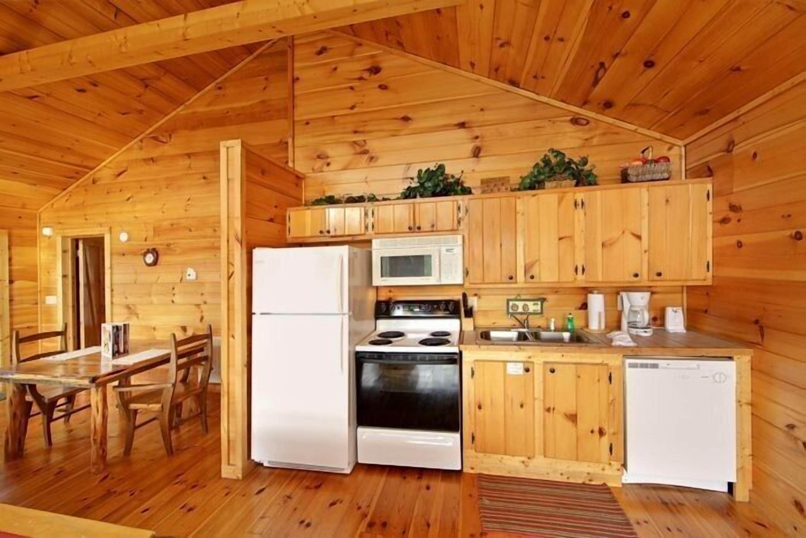 A wooden cabin interior with a kitchen featuring a refrigerator, stove, microwave, and sink.