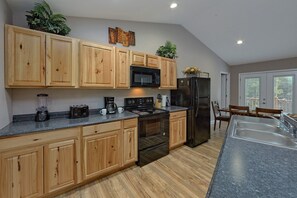 A kitchen with wooden cabinets, a black refrigerator, a microwave, and a stove. - Bearfoot Bungalow | Hot Tub | Close to Dollywood | Free Attraction Tickets (Pigeon Forge)