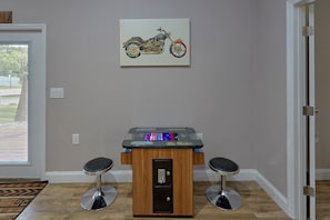 Une pièce comprenant une table de baby-foot, deux tabourets, une œuvre d’art représentant une moto accrochée au mur, et une porte.