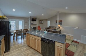 A modern kitchen with a central island, wooden cabinets, and a built-in dishwasher. - Bearfoot Bungalow | Hot Tub | Close to Dollywood | Free Attraction Tickets (Pigeon Forge)