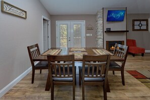 A dining room with a wooden table and chairs, a TV mounted on the wall, and a fireplace. - Bearfoot Bungalow | Hot Tub | Close to Dollywood | Free Attraction Tickets (Pigeon Forge)