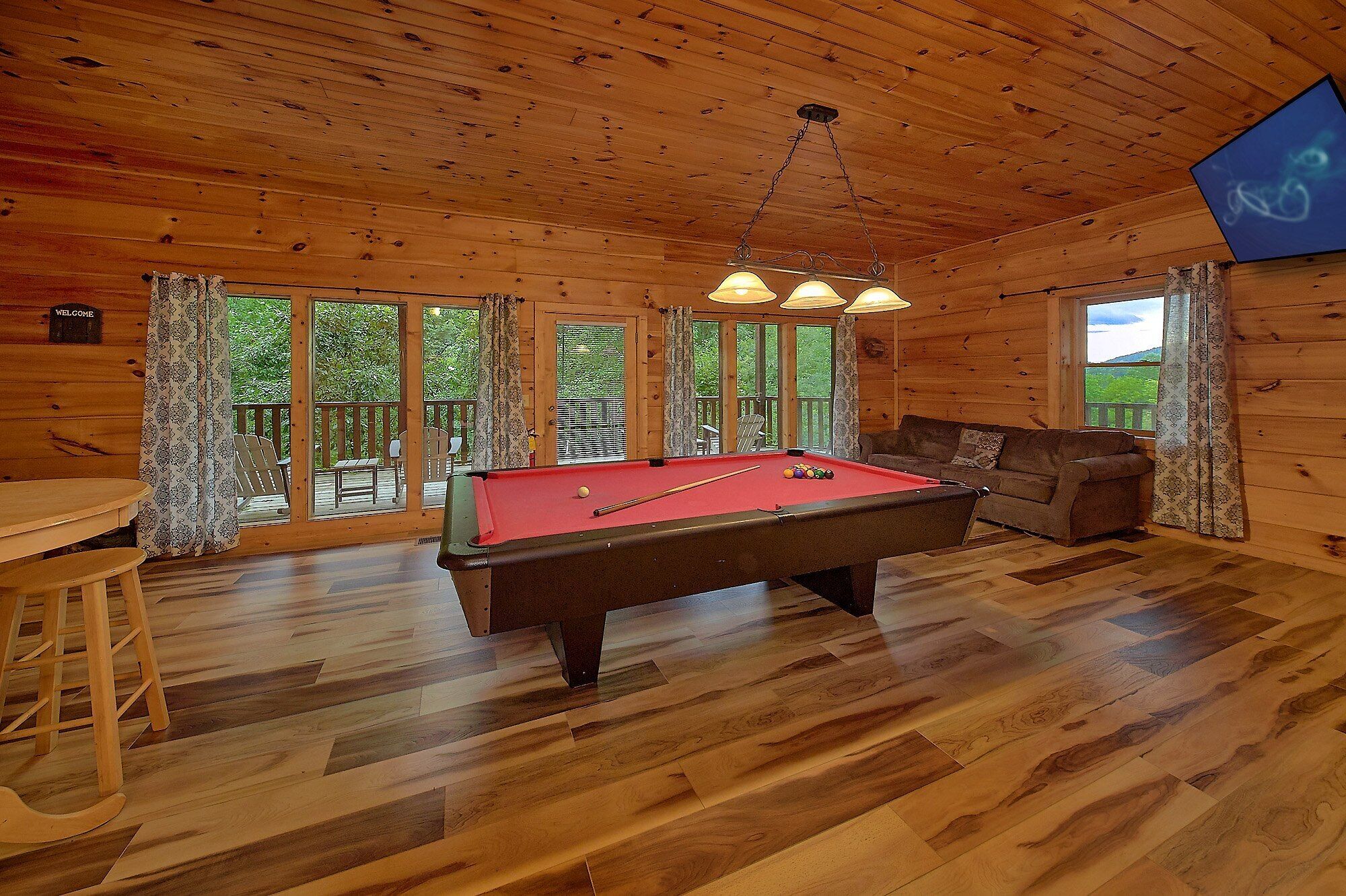 A wooden cabin with a pool table, a sofa, and a dining area.
