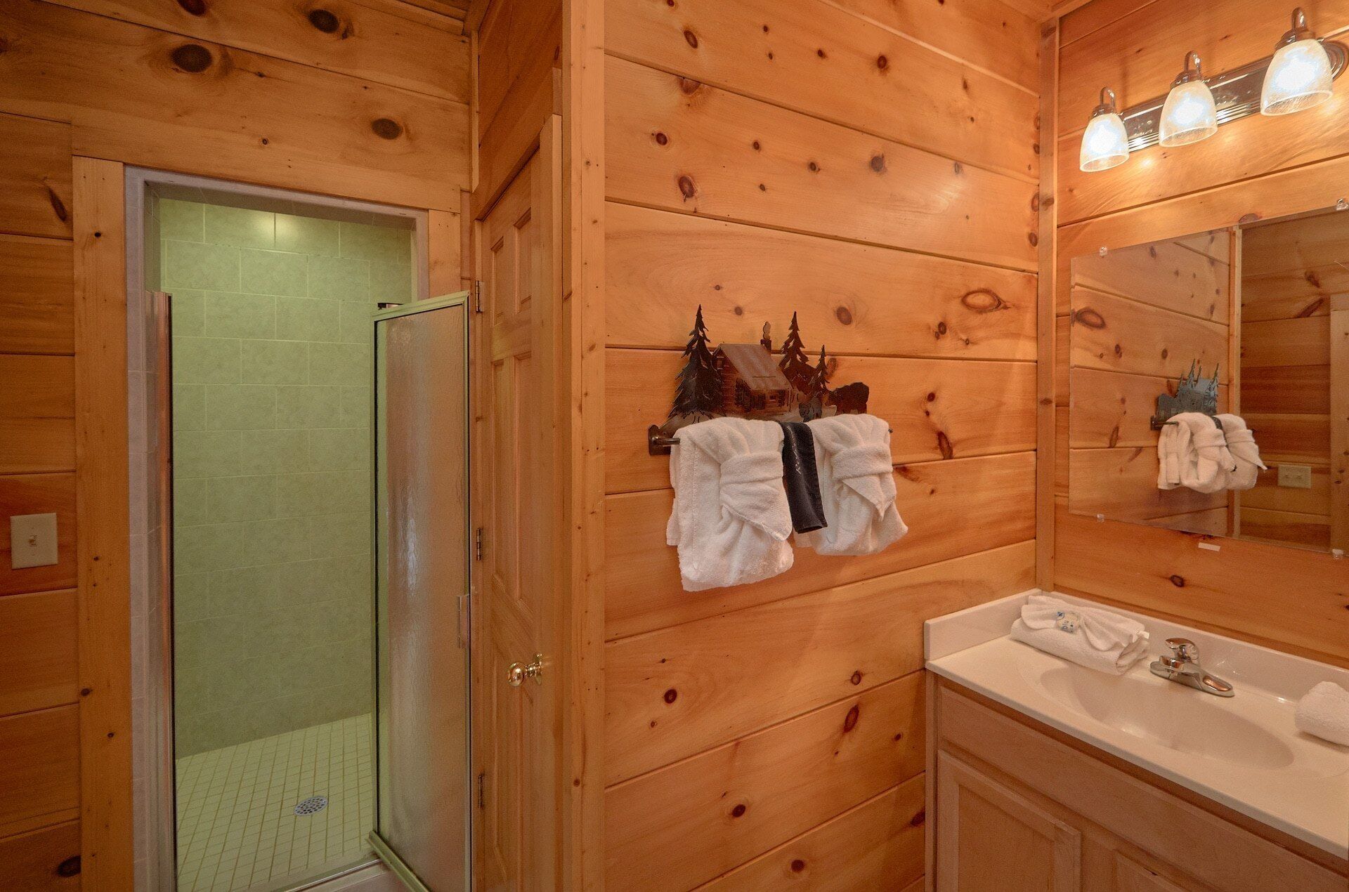 Een badkamer met houten lambrisering, een glazen douchedeur, een wastafel en een handdoekrek met handdoeken.