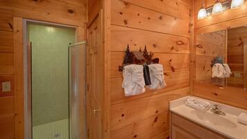 Een badkamer met houten lambrisering, een glazen douchedeur, een wastafel en een handdoekrek met handdoeken.
