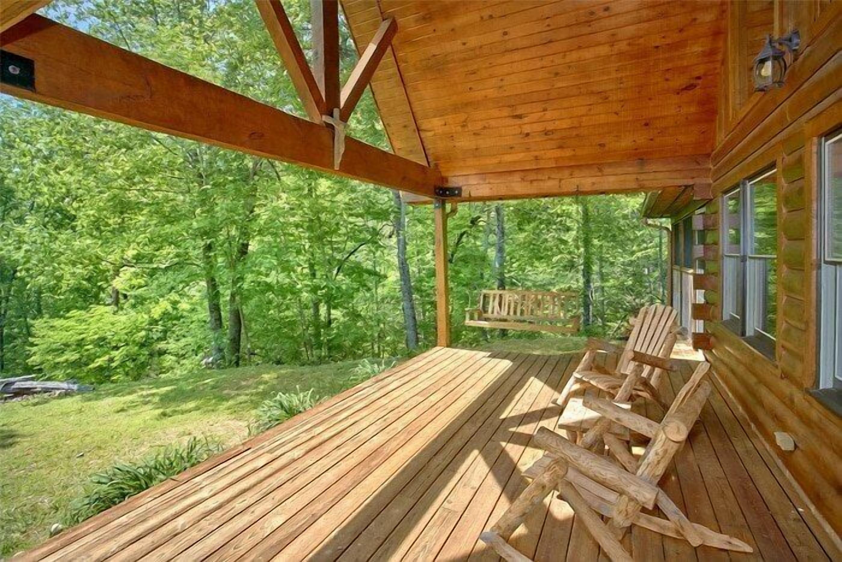 A wooden deck with chairs, a bench, and a view of a forest.