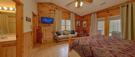 Una habitación con cama, televisor, cómoda de madera, silla y ventilador de techo.