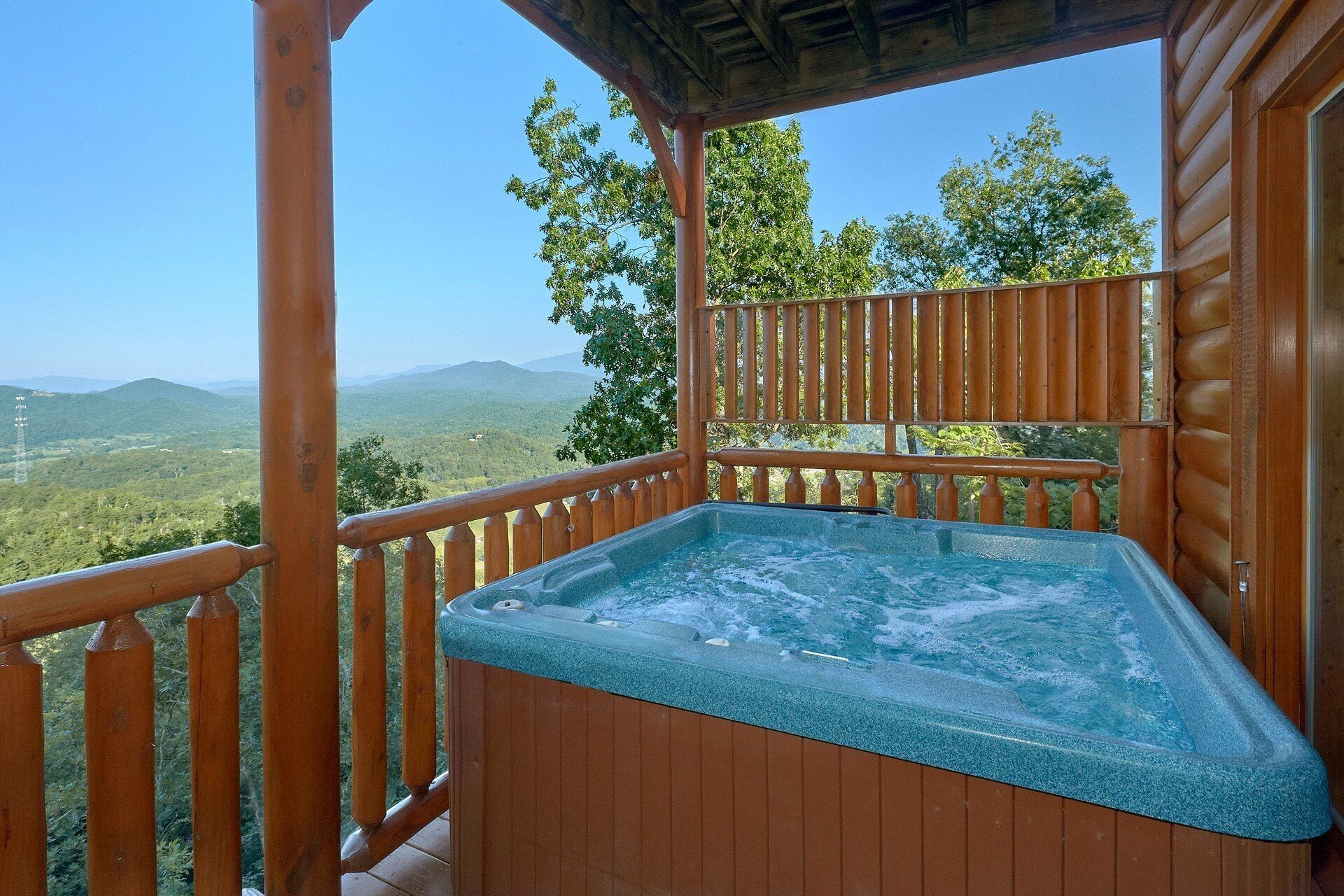 Een houten terras met een jacuzzi en uitzicht op een bergachtig landschap.