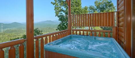 Terraza de madera con hidromasaje y vistas a un paisaje montañoso.