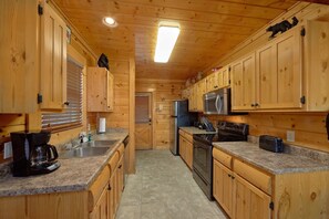 Ein Holzblockhaus-Interieur mit einer Küche, die sich durch Granitarbeitsplatten, Holzschränke, einen Kühlschrank, eine Mikrowelle und einen Herd auszeichnet.