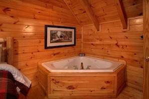 A wooden cabin interior with a large wooden bathtub, a framed picture on the wall, and a door. - Catch of the Day | Mtn Views, Hot Tub, Game Room, Pigeon Forge, Fireplace + Free Attraction Tickets (Pigeon Forge)