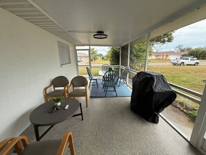 Un patio cubierto con mesa, sillas, una parrilla y vistas al exterior.
