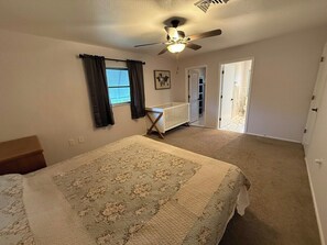 A bedroom with a bed, a ceiling fan, a window with curtains, and a door leading to a bathroom. - The Manasota Retreat - Steps from Lemon Bay Park, Private Lanai w/ BBQ (Englewood)