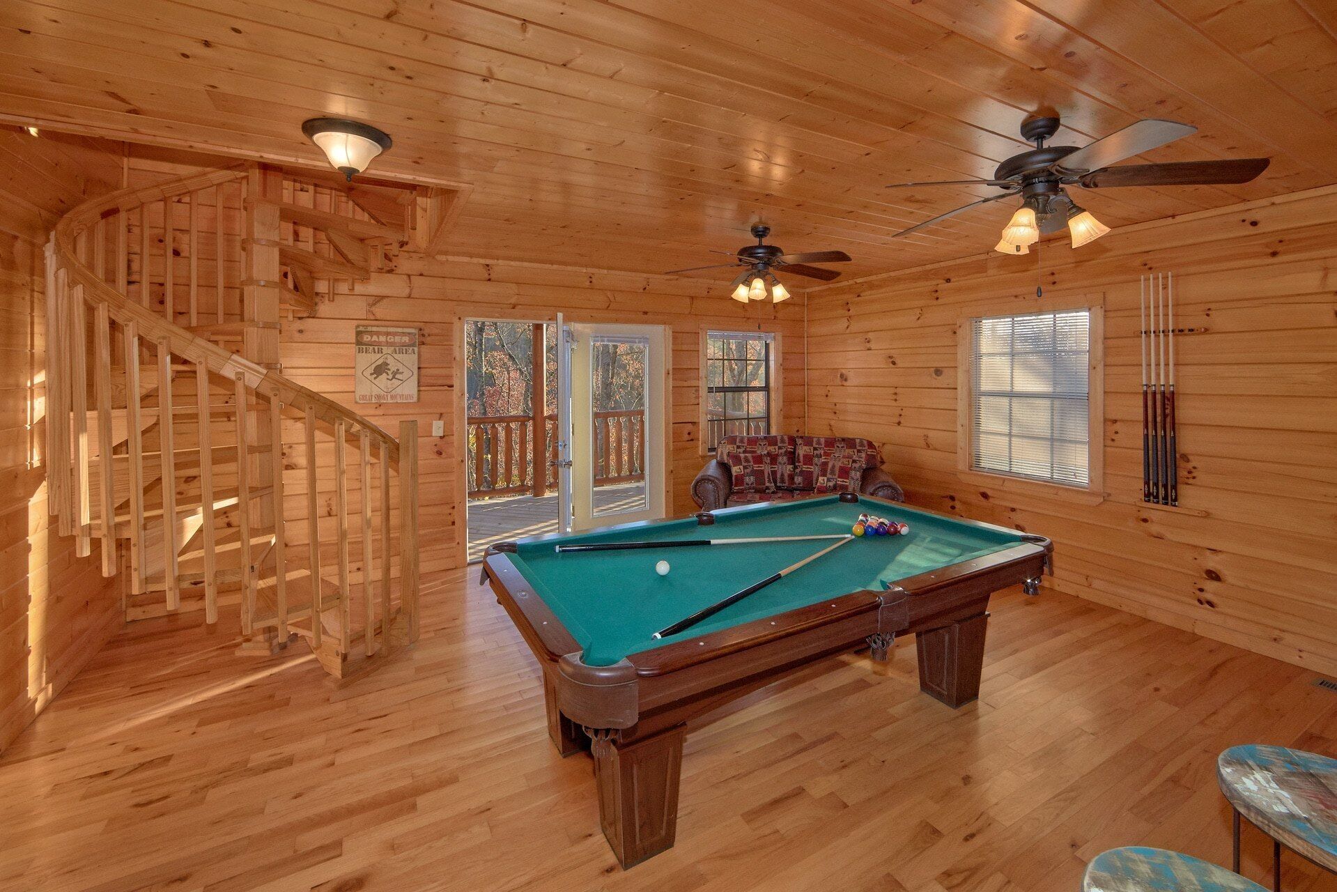 A wooden interior with a pool table, a staircase, and a ceiling fan.