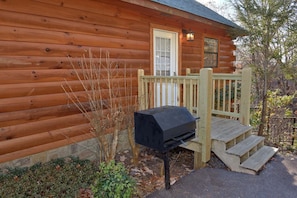 A wooden cabin with a front door, a small porch, and a barbecue grill. - Cheeky Chipmunk Getaway (Sevierville)