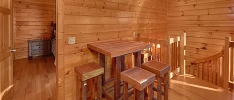 Un interior de madera con una mesa de comedor y cuatro taburetes, una escalera y una puerta que da a otra habitación.