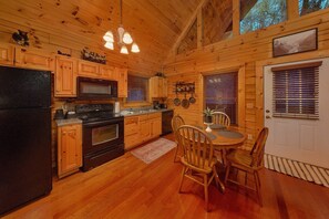 A wooden cabin interior with a kitchen, dining area, and a door with blinds. - Lion's Den | Hot Tub, Game Room, Sauna, Pigeon Forge, Fireplace + Free Attraction Tickets (Pigeon Forge)