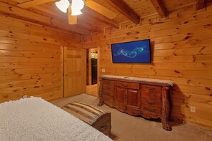 A wooden-paneled room with a bed, a dresser, and a television mounted on the wall. - Lion's Den | Hot Tub, Game Room, Sauna, Pigeon Forge, Fireplace + Free Attraction Tickets (Pigeon Forge)