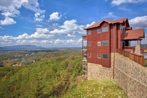 Ein mehrstöckiges Blockhaus mit Steinunterbau, einem Balkon und Blick auf eine gebirgige Landschaft.
