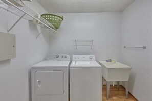 Ein Waschraum mit zwei weißen Waschmaschinen und Trocknern, einem kleinen Waschbecken und einem grünen Wäschekorb auf einem Regal.