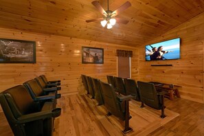 A wooden-paneled room with a ceiling fan, a television mounted on the wall, and rows of seating.