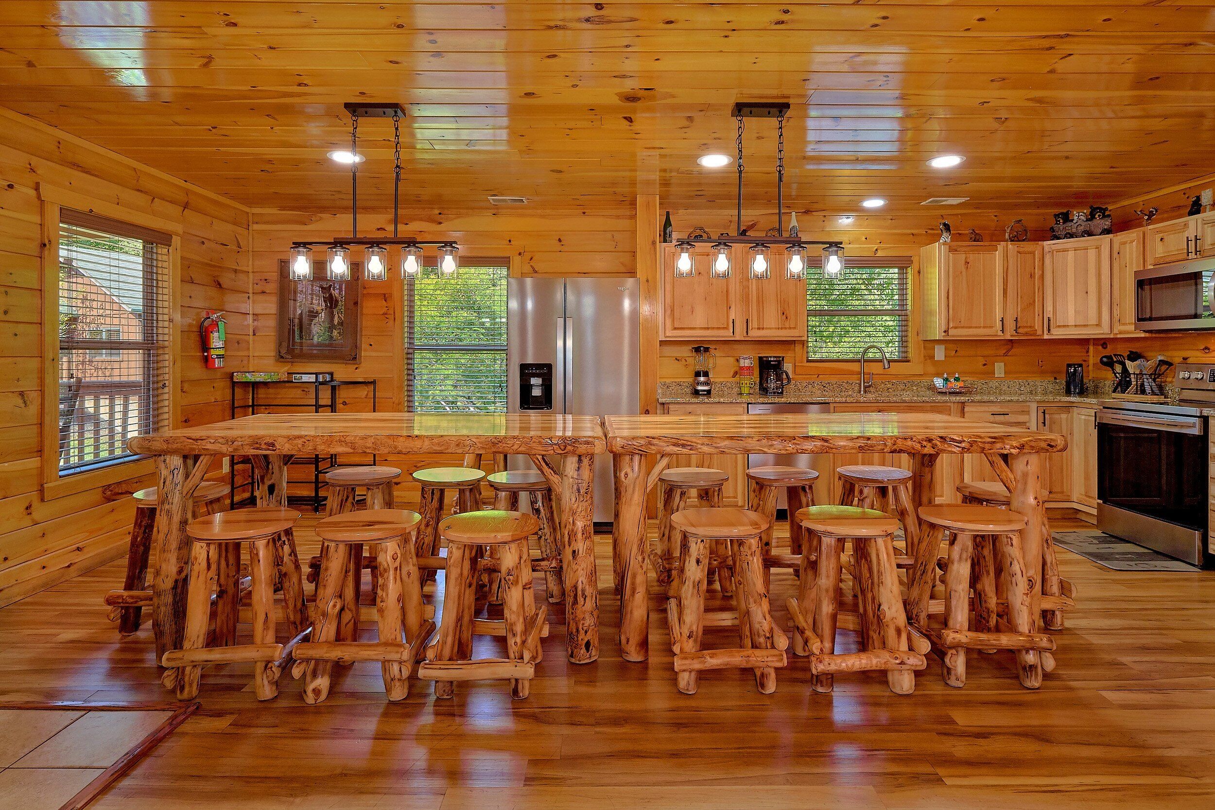 A wooden cabin interior with a central island bar, wooden stools, and a kitchen area with wooden cabinets and appliances.