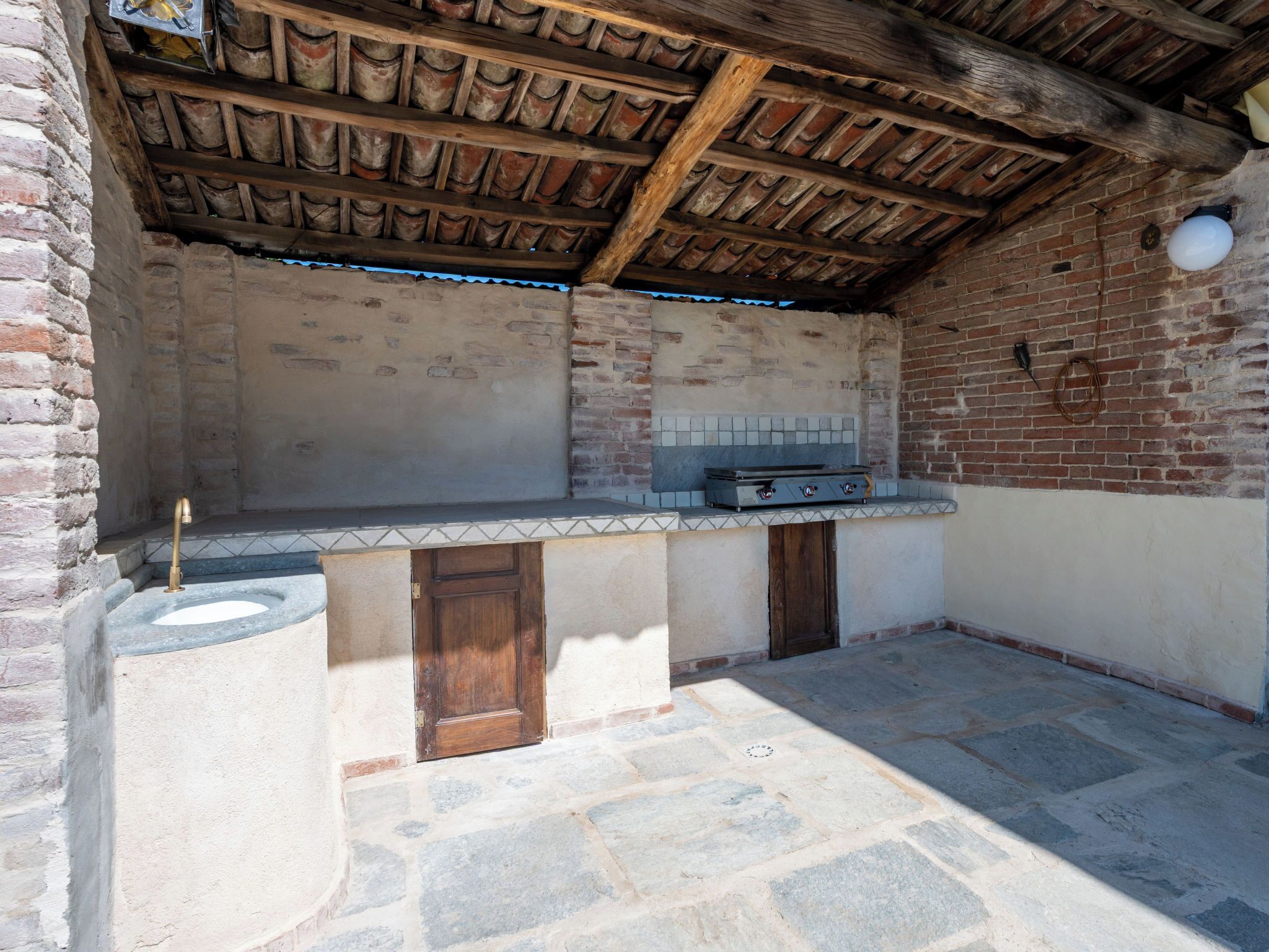 Un espace cuisine extérieur avec un mur en briques, un sol en pierre et un plafond en bois.