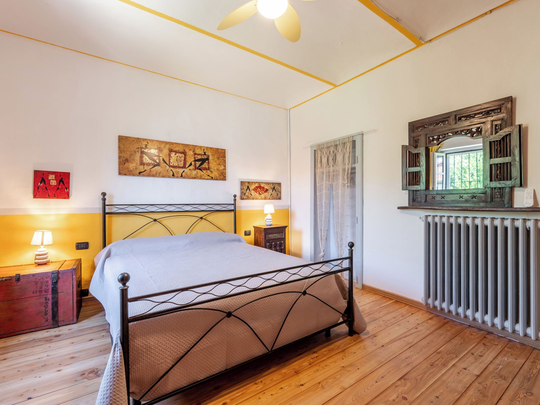 Une chambre avec un lit en métal, un plancher en bois, un radiateur et des œuvres d’art accrochées au mur.