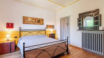 Une chambre avec un lit en métal, un plancher en bois, un radiateur et des œuvres d’art accrochées au mur.