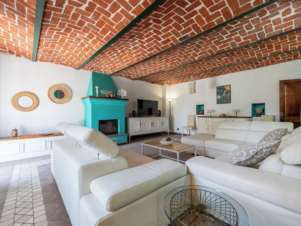 A living room with a brick ceiling, white sofas, a teal fireplace, and a TV.