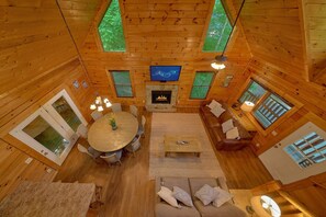 A cozy cabin interior with a fireplace, a television, and a dining area with a round table and chairs. - Cuddly Critters | Hot Tub, Game Room, Sleeps 12, Pigeon Forge, Fireplace + Free Attraction Tickets (Pigeon Forge)