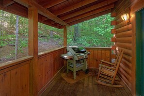 A wooden cabin with a grill and a rocking chair. - Cuddly Critters | Hot Tub, Game Room, Sleeps 12, Pigeon Forge, Fireplace + Free Attraction Tickets (Pigeon Forge)