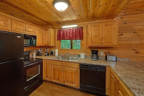 A wooden cabin kitchen with a refrigerator, stove, sink, and dishwasher. - Cuddly Critters | Hot Tub, Game Room, Sleeps 12, Pigeon Forge, Fireplace + Free Attraction Tickets (Pigeon Forge)