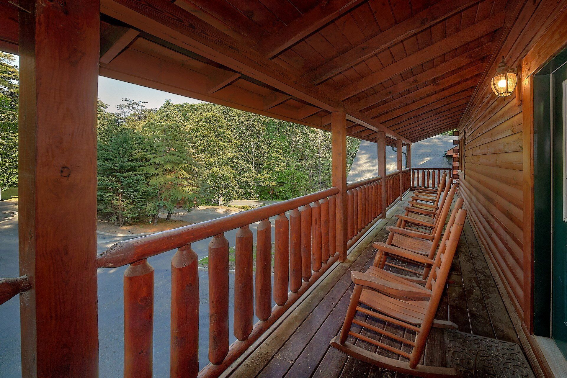 Ein Holzbalkon mit Geländer, Holzstühlen und Blick auf Bäume und eine Straße.
