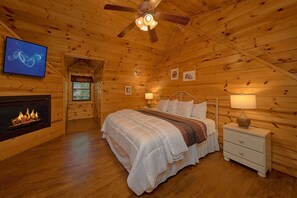 A cozy log cabin bedroom with a bed, bedside tables, a fireplace, and a ceiling fan. - Cuddly Critters | Hot Tub, Game Room, Sleeps 12, Pigeon Forge, Fireplace + Free Attraction Tickets (Pigeon Forge)