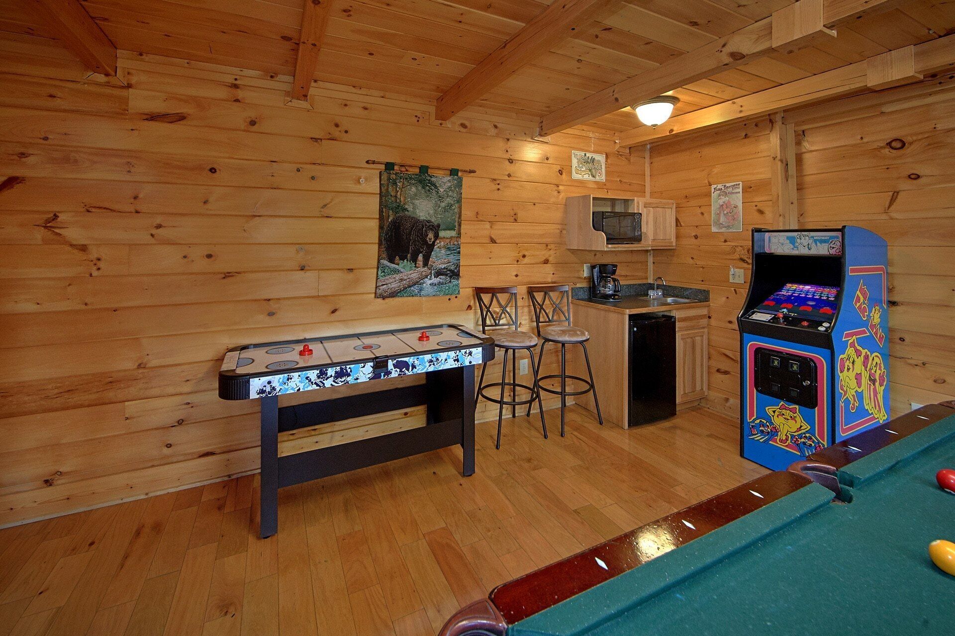 A room with a foosball table, a pool table, and a pinball machine.