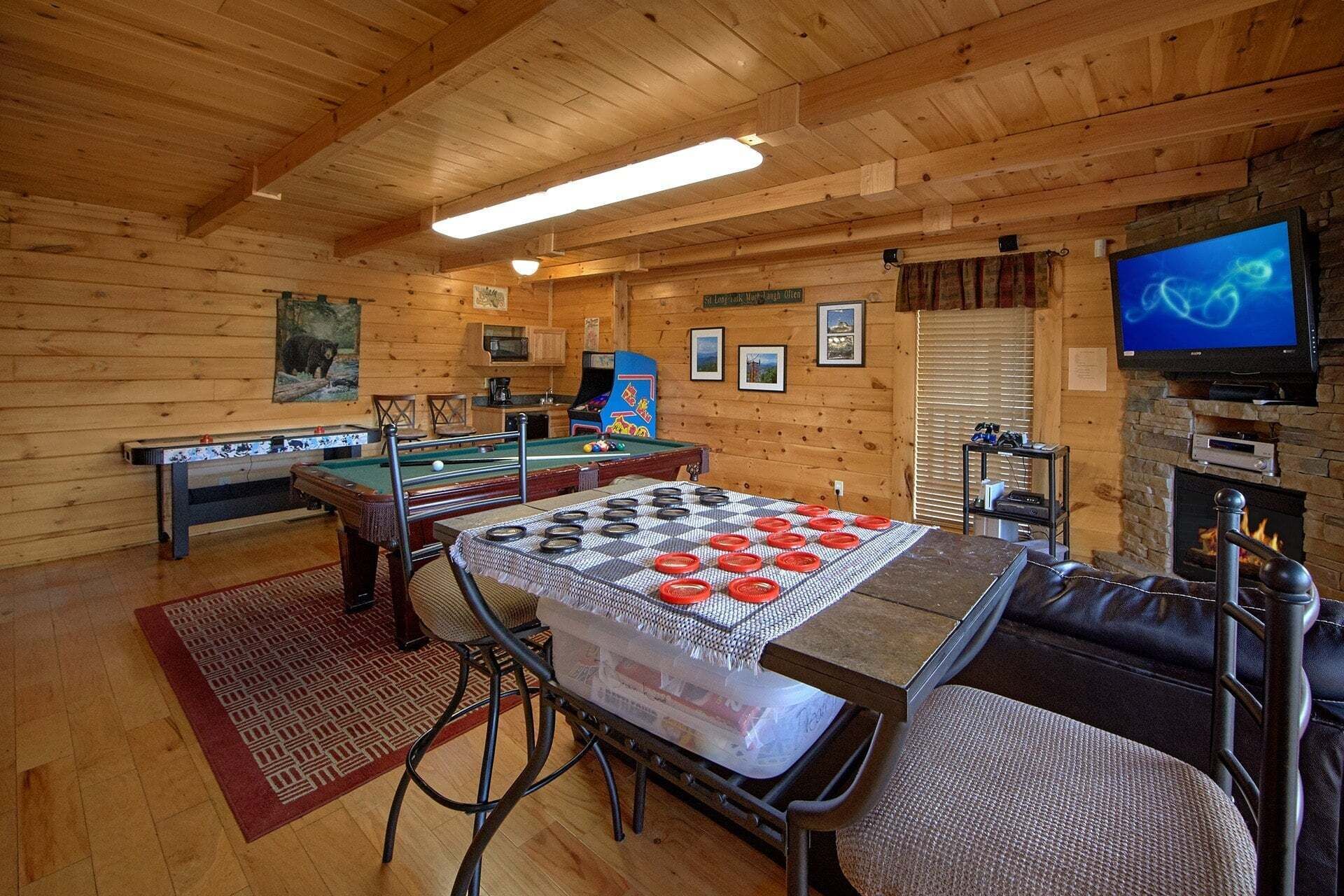 A wooden interior with a pool table, a foosball table, a billiards table, a television, and a fireplace.