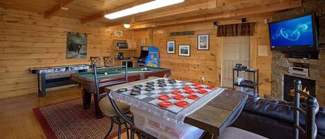 A wooden interior with a pool table, a foosball table, a billiards table, a television, and a fireplace.