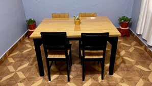 A dining area with a wooden table and black chairs, surrounded by potted plants.