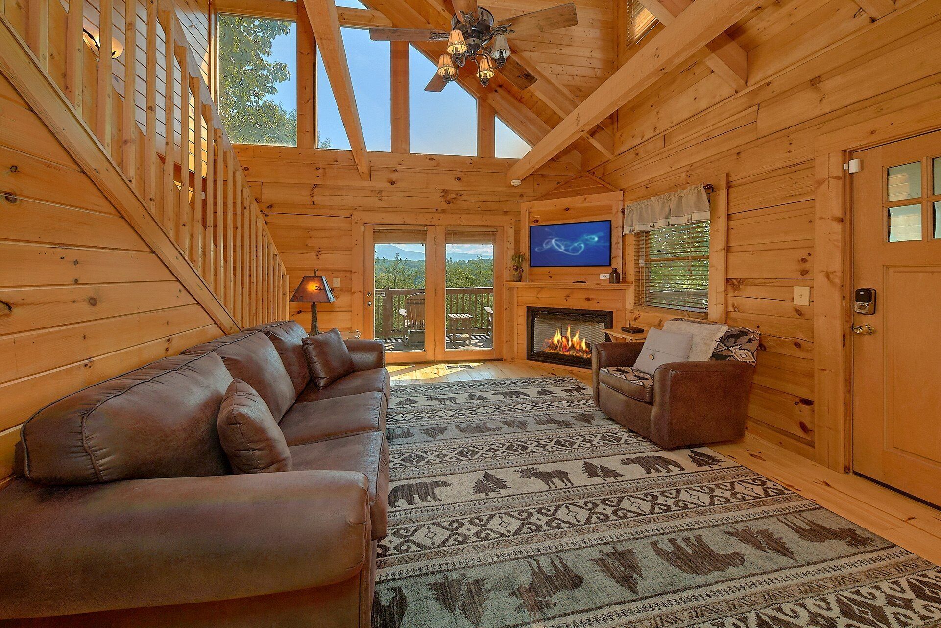L’intérieur d’un chalet en bois comprend un canapé, un fauteuil, une cheminée, un téléviseur et une vue sur l’extérieur à travers les portes vitrées.
