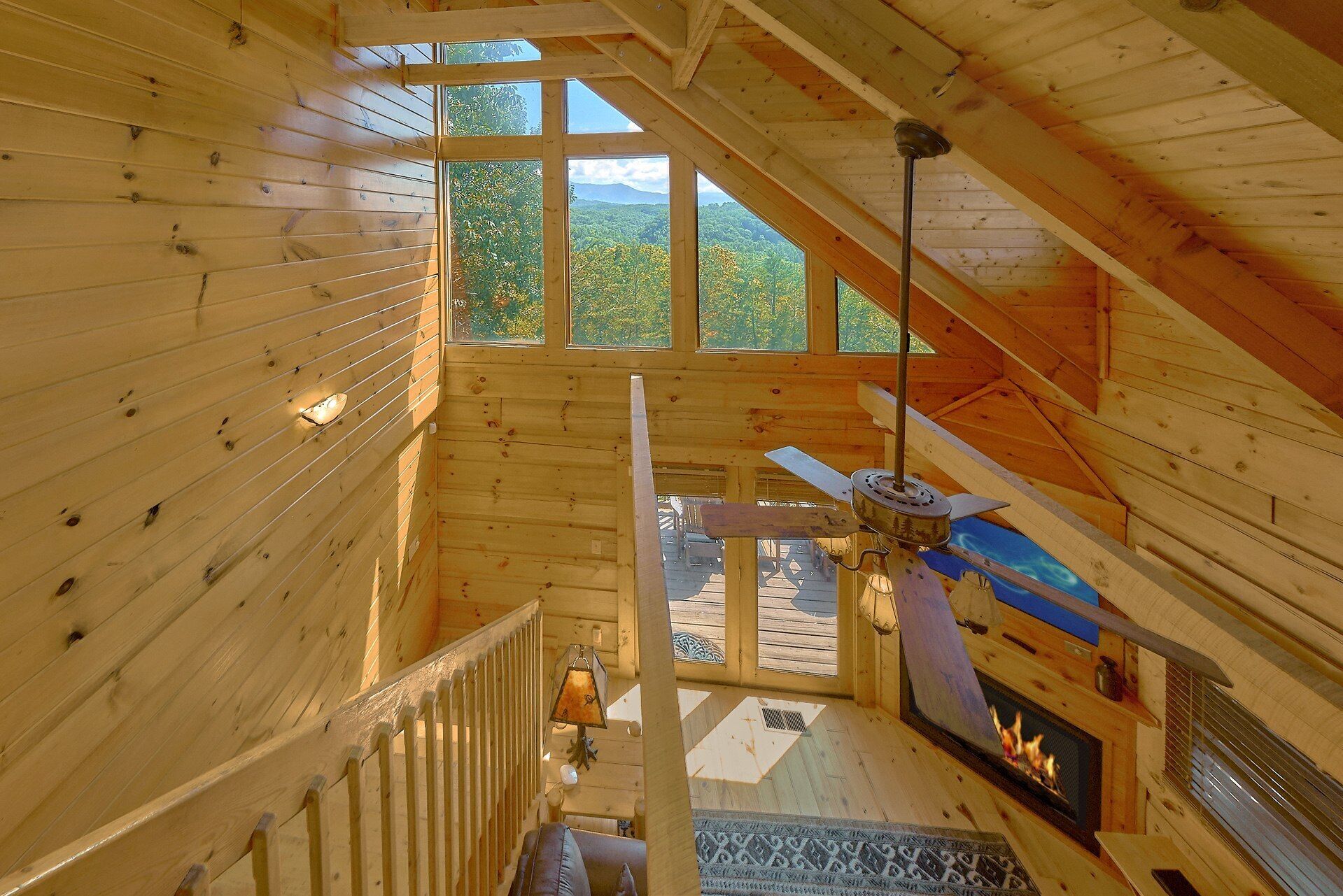 A wooden cabin interior with a fireplace, a ceiling fan, and a view of the outdoors.