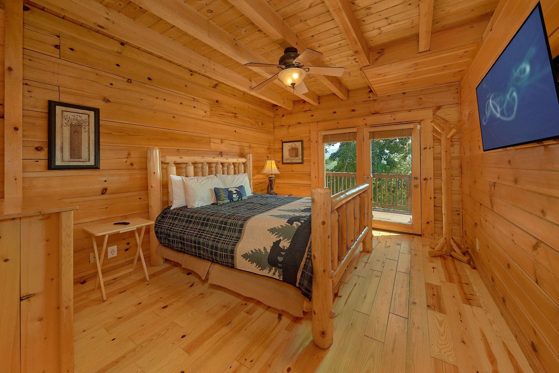 Une chambre dans une cabane en bois, avec un lit, une table de chevet, un ventilateur de plafond et une fenêtre donnant sur la verdure.
