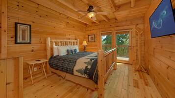 Une chambre dans une cabane en bois, avec un lit, une table de chevet, un ventilateur de plafond et une fenêtre donnant sur la verdure.