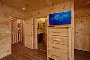 Ein Holzinterieur mit einem Fernseher auf einem Schrank, ein Badezimmer mit Waschbecken und Spiegel sowie eine Holztür.